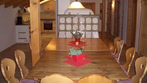 A wooden dining table with chairs, a central floral arrangement, and a kitchen in the background.