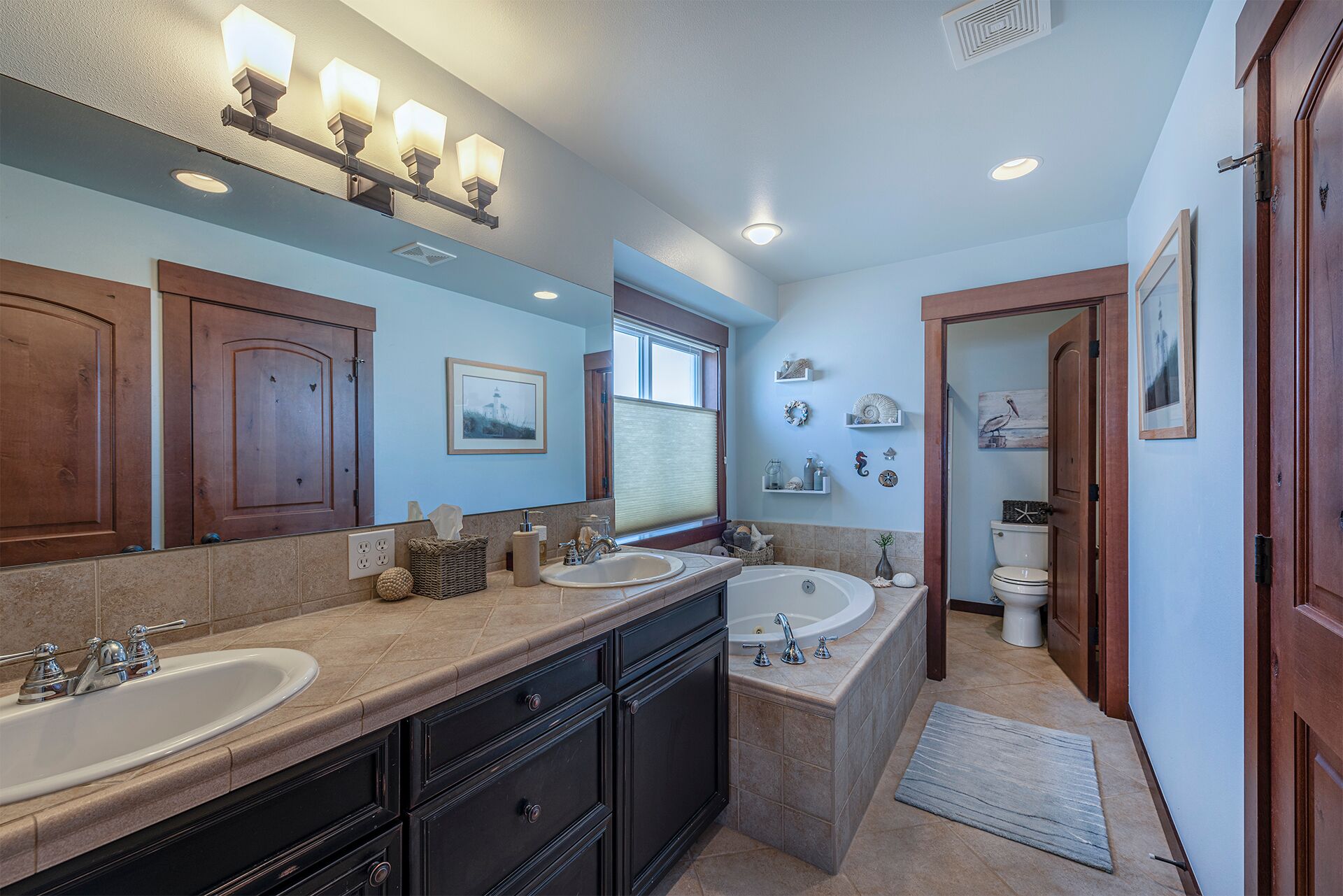 A bathroom with two sinks, a bathtub, wooden cabinets, and a window.