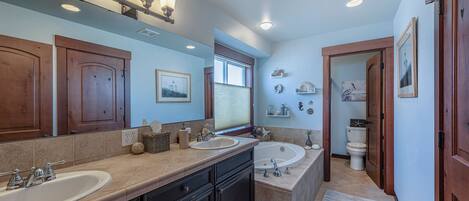 A bathroom with two sinks, a bathtub, wooden cabinets, and a window.