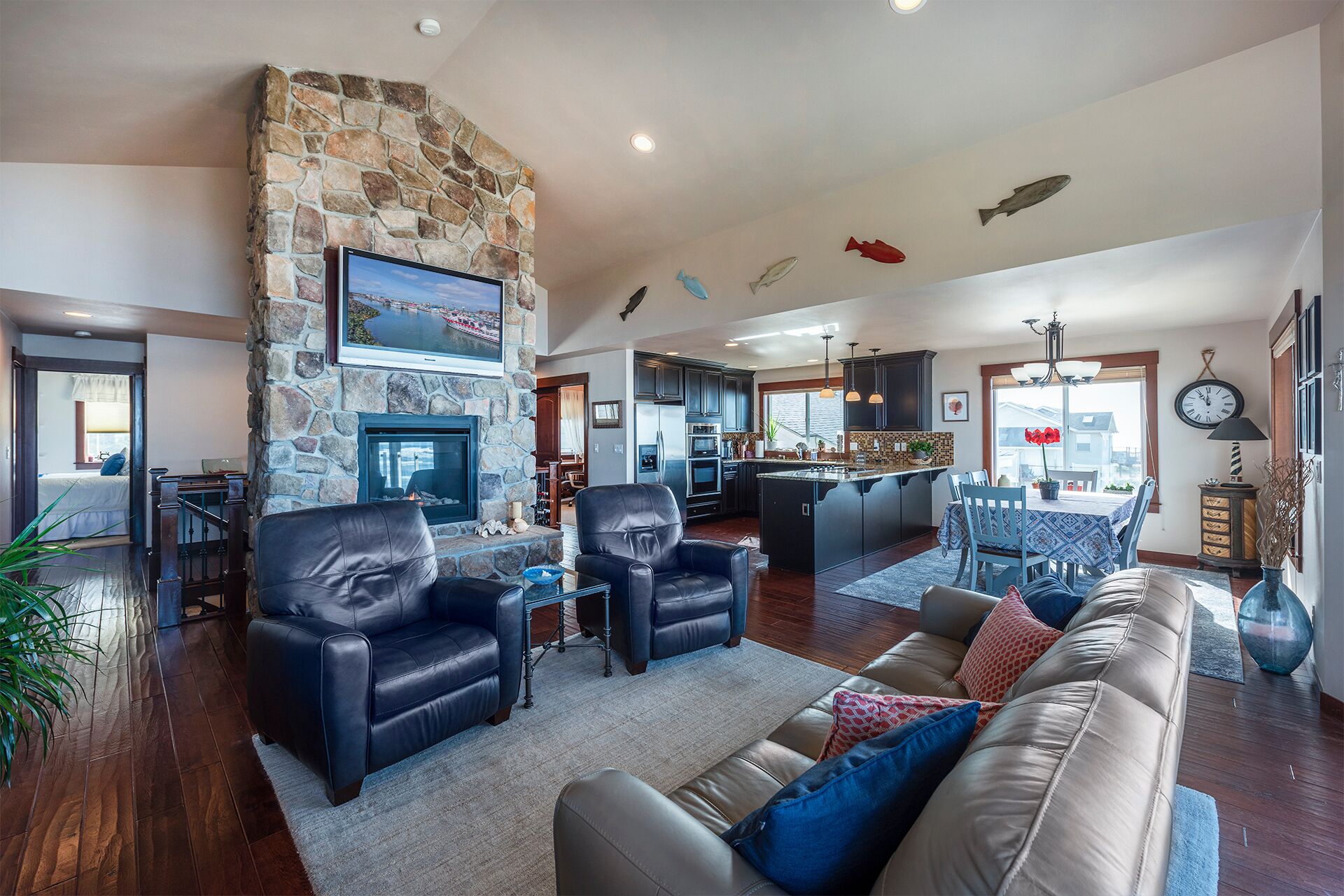 A spacious living room with a stone fireplace, leather sofas, and a kitchen in the background.