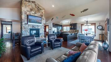 A spacious living room with a stone fireplace, leather sofas, and a kitchen in the background.