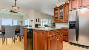 Een moderne keuken met houten kastjes, een roestvrijstalen koelkast en een eetgedeelte met een groot eiland en stoelen.
