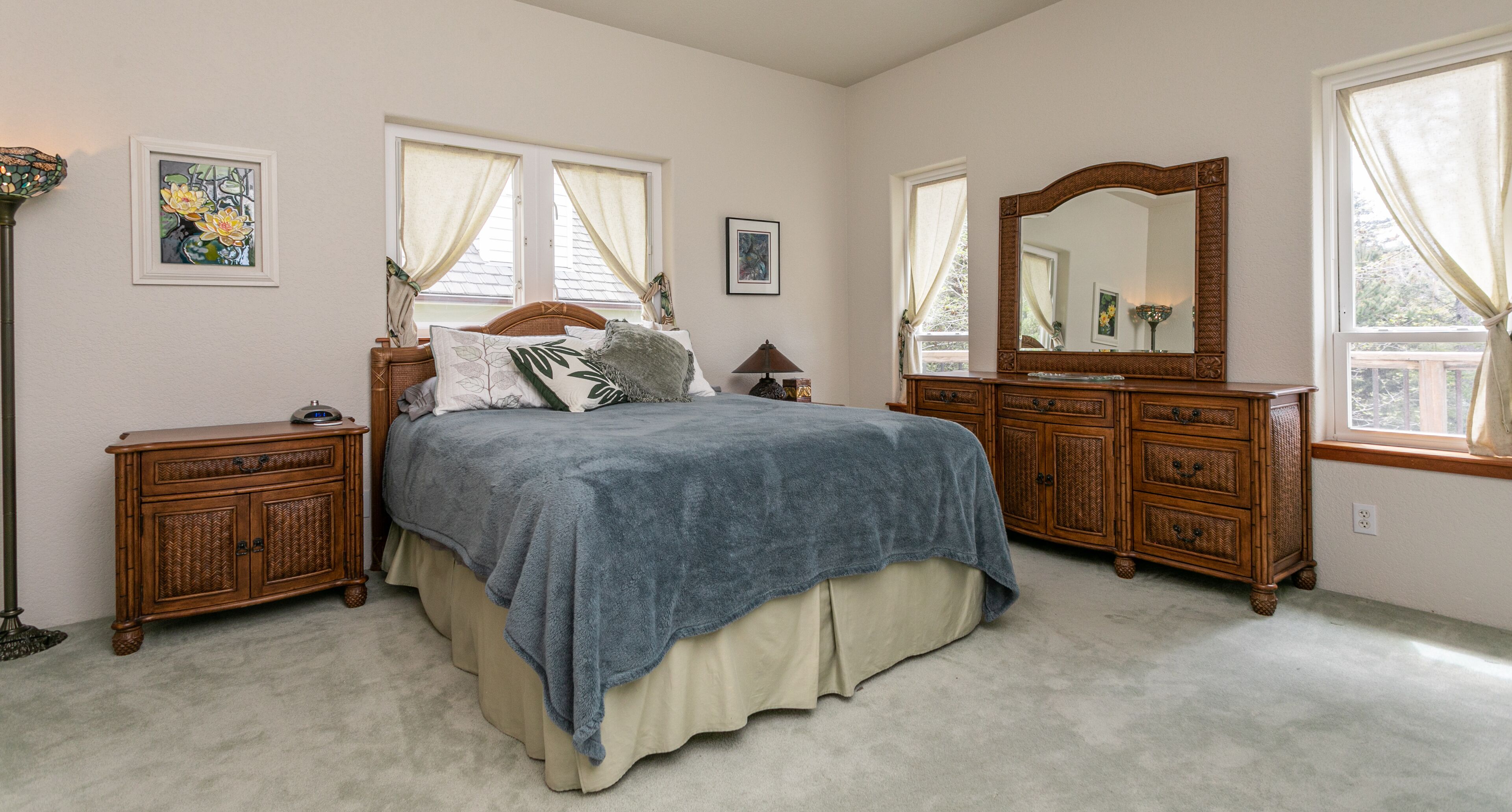 A bedroom with a bed, two nightstands, a dresser, a mirror, and two windows with curtains.