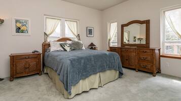 A bedroom with a bed, two nightstands, a dresser, a mirror, and two windows with curtains.