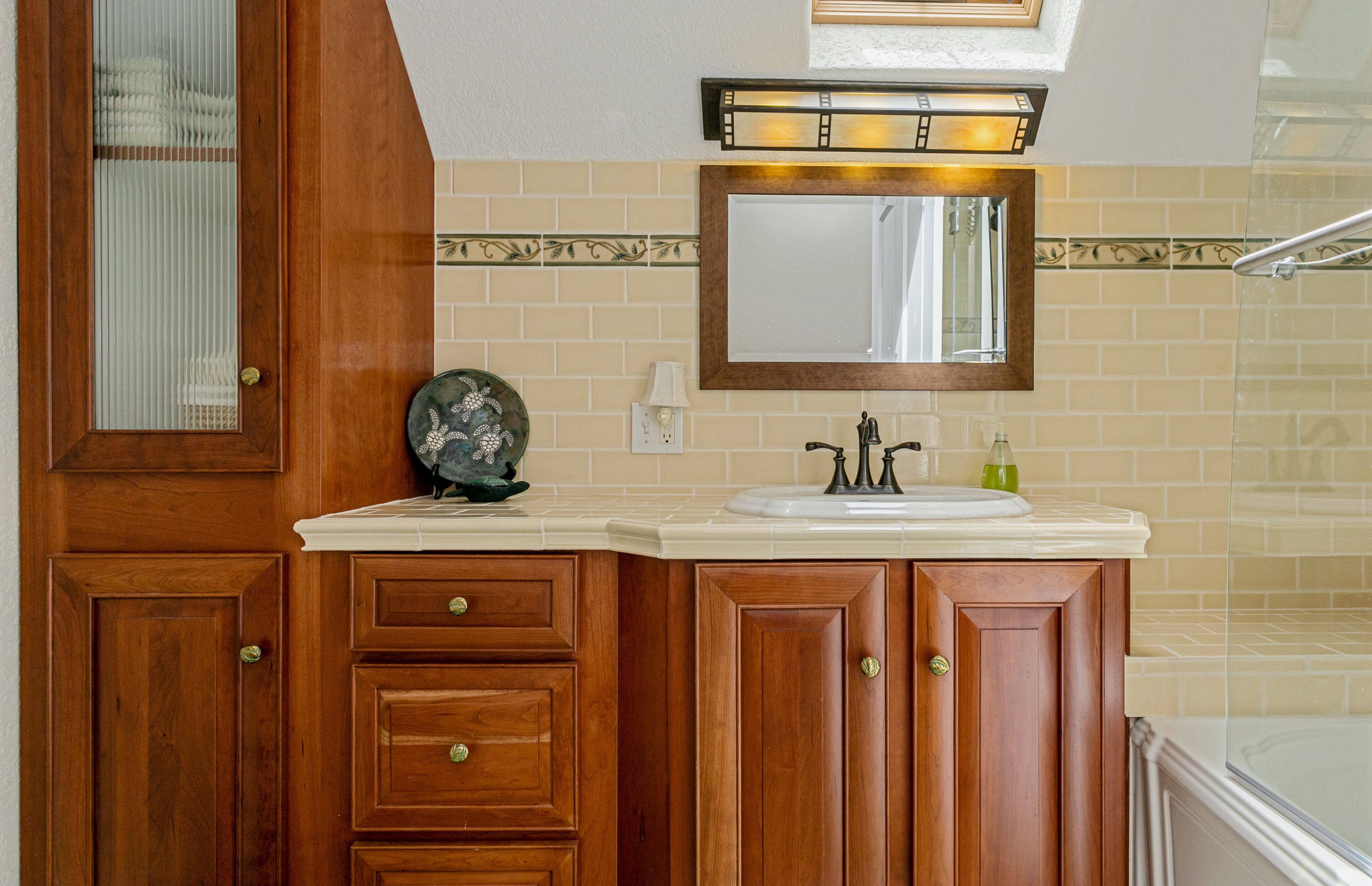 A bathroom with wooden cabinets, a sink, a mirror, and a shower area.