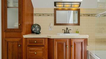 A bathroom with wooden cabinets, a sink, a mirror, and a shower area.