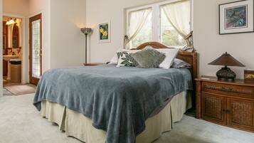 A bedroom with a large bed, a wooden nightstand, a lamp, and a window with curtains.