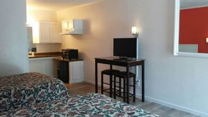 A room with two beds, a desk with a chair, a TV, and a kitchen area in the background. - Unity Lodge Suite 2 (Golconda)