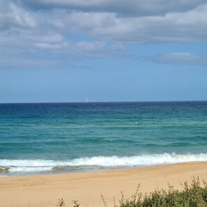 Une plage avec une eau d’un bleu limpide et un navire qui se profile à l’horizon.