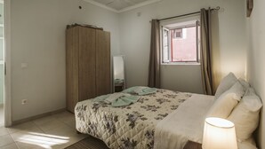 Een slaapkamer met een bed, een kledingkast, een raam en een lamp.