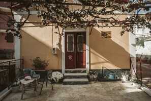 Eine Villa mit Holztür, einer kleinen Veranda mit Stuhl und Tisch sowie einem Blumentopf.