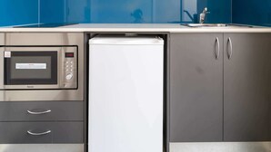 Una cocina compacta con gabinetes grises, un microondas integrado y un refrigerador blanco.