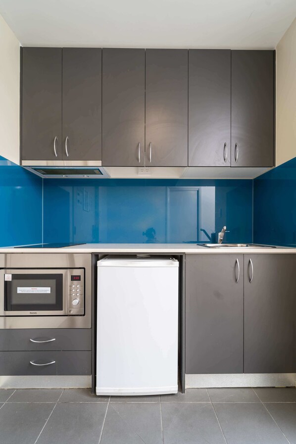 A compact kitchen with grey cabinets, a built-in microwave, and a white refrigerator.