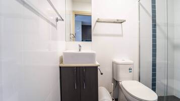 A modern bathroom with a white sink, dark cabinet, toilet, and glass shower enclosure.