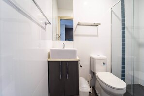 A modern bathroom with a white sink, dark cabinet, toilet, and glass shower enclosure. - Dayman Apartments (Marsfield)