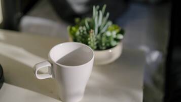A white mug on a table with a small potted plant in the background.