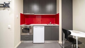 Cocina compacta con armarios grises, salpicadero rojo, horno empotrado y lavavajillas blanco.