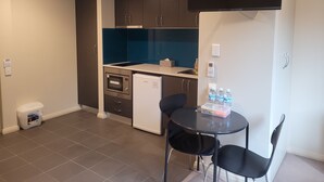 Cocina compacta con armarios oscuros, microondas, refrigerador pequeño, pileta y una mesa negra con dos sillas.