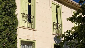 A building with green shutters, a balcony with wrought iron railings, and a potted plant in the foreground. - Mas des Marbres Sauvages propriété 36 personnes (Sainte-Marie-la-Mer)