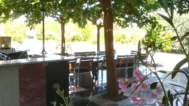 A glass-enclosed outdoor seating area with tables and chairs, surrounded by greenery and a water feature. - Mas des Marbres Sauvages propriété 36 personnes (Sainte-Marie-la-Mer)