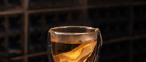 A clear glass cup with a tea bag on a reflective surface, steam rising from it, against a dark background with a grid pattern.