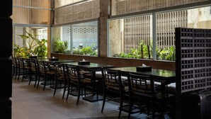Comedor con varias mesas y sillas, ventanas amplias con rejas de metal y plantas en macetas.