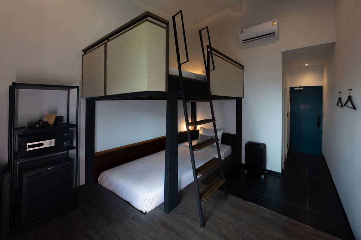 A compact hotel room with a bunk bed, a desk with a computer, and a small trash bin.