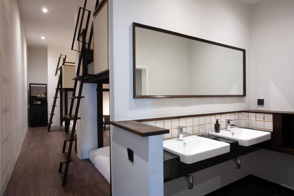 A modern bathroom with two sinks, a large mirror, and a wooden ladder.
