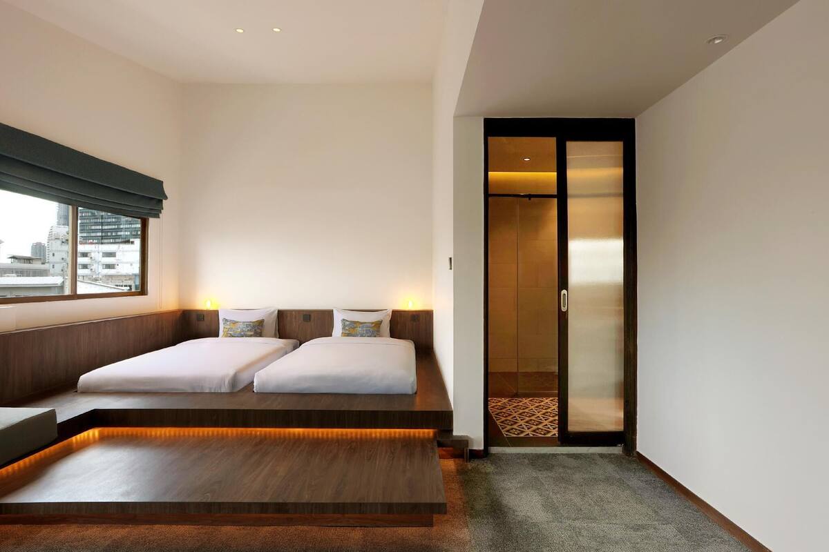 A modern hotel room with a large bed, a desk, and a view of the city through the window.