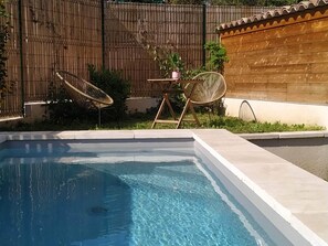 Una piscina con una valla de madera y dos sillas de mimbre.