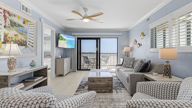Un salón amplio con ventilador de techo, televisor grande y balcón con vistas.