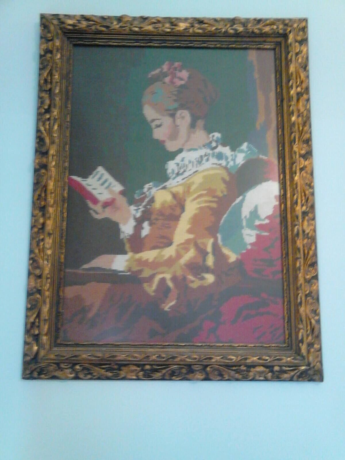 A framed painting of a woman reading a book.