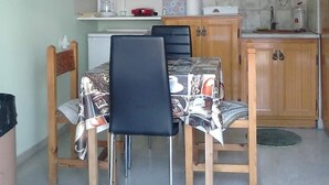 A compact kitchen with wooden cabinets, a dining table with chairs, and a refrigerator. - Vasiliki's Apartment (Kalampaka center) (ΚΑΛΑΜΠΑΚΑ ΜΕΤΕΩΡΩΝ)
