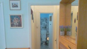 A narrow hallway with a wooden bench, a door leading to a bathroom, and a mirror reflecting a plant. - Vasiliki's Apartment (Kalampaka center) (ΚΑΛΑΜΠΑΚΑ ΜΕΤΕΩΡΩΝ)