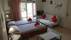 A hotel room with two beds, a sofa, a glass coffee table, and a TV. - Vasiliki's Apartment (Kalampaka center) (ΚΑΛΑΜΠΑΚΑ ΜΕΤΕΩΡΩΝ)