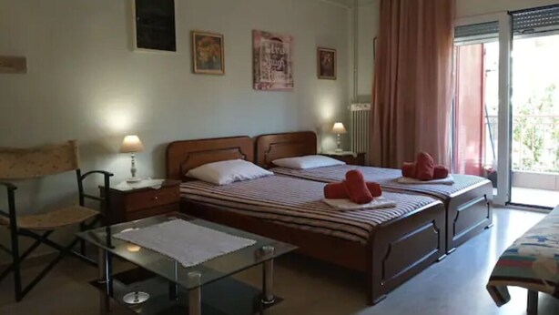 A hotel room with two beds, a desk, a chair, and a window with curtains. - Vasiliki's Apartment (Kalampaka center) (ΚΑΛΑΜΠΑΚΑ ΜΕΤΕΩΡΩΝ)