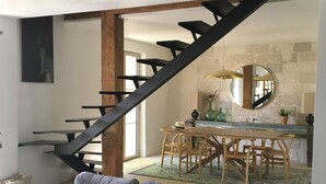 Ein modernes Wohnzimmer mit einem grauen Sofa, einem Holzesstisch mit Stühlen und einer schwarzen Treppe, die in einen anderen Raum führt.