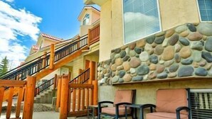 A building with a stone facade, a wooden staircase, and outdoor seating. - 3-Story Condo / Mountain Views / Board Games (Fernie)
