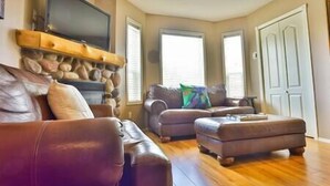 A living room with a stone fireplace, leather sofas, and a flat-screen TV. - 3-Story Condo / Mountain Views / Board Games (Fernie)