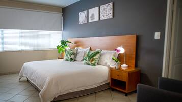 A neatly made bed with a wooden headboard, a bedside table with a lamp, and a potted plant.