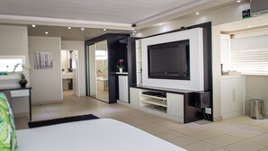 Une chambre moderne avec un grand lit, un téléviseur fixé au mur et un petit coin cuisine.