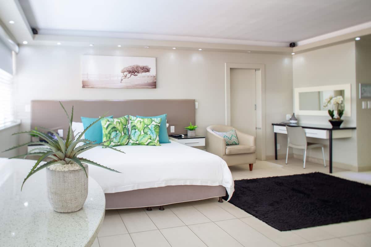 A modern bedroom with a bed, bedside table, potted plant, and a desk with a chair.