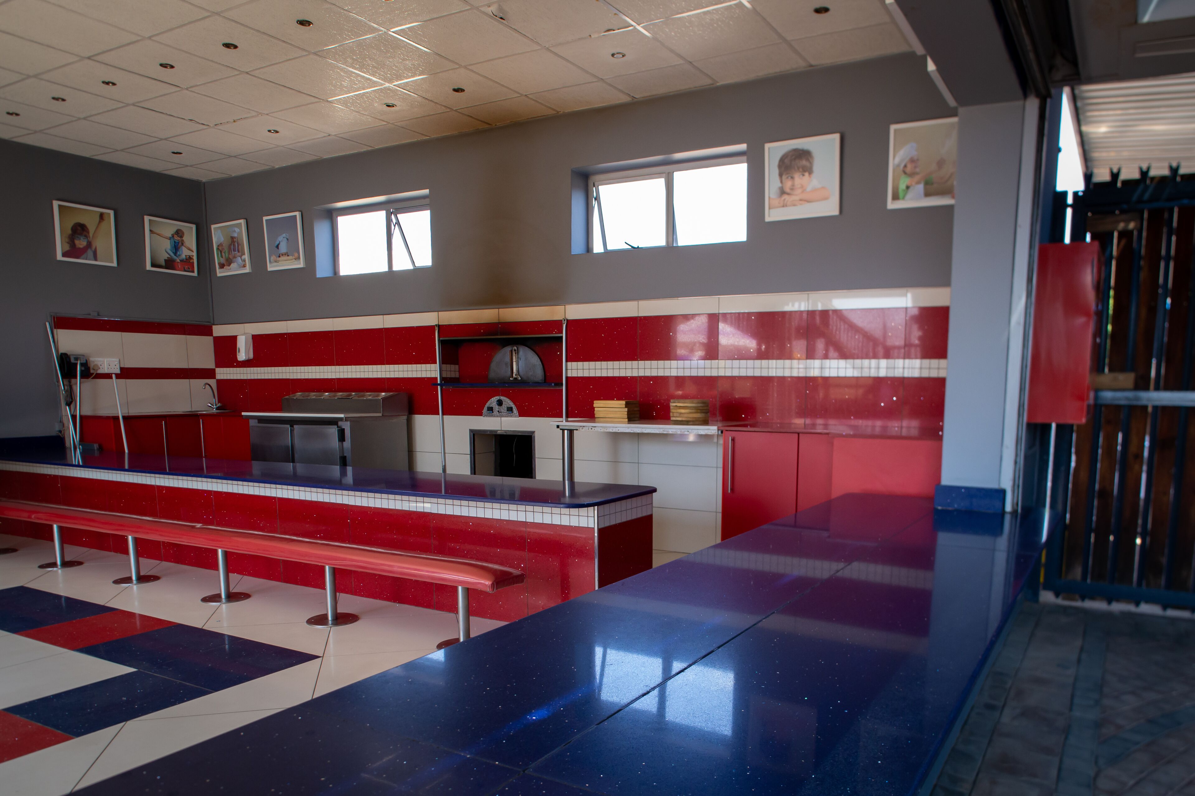 A spacious kitchen with red and white tiled walls, a long counter, and a stainless steel sink.