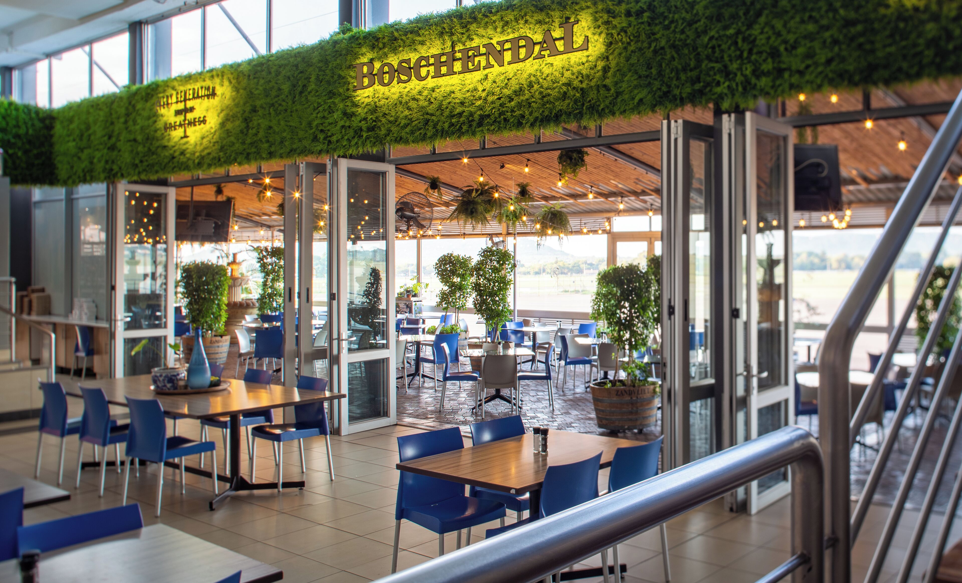 A restaurant with a green wall and the name 'BOSCHENDAHL' in gold letters. There are tables and chairs inside, and a view of the outdoors through large windows.