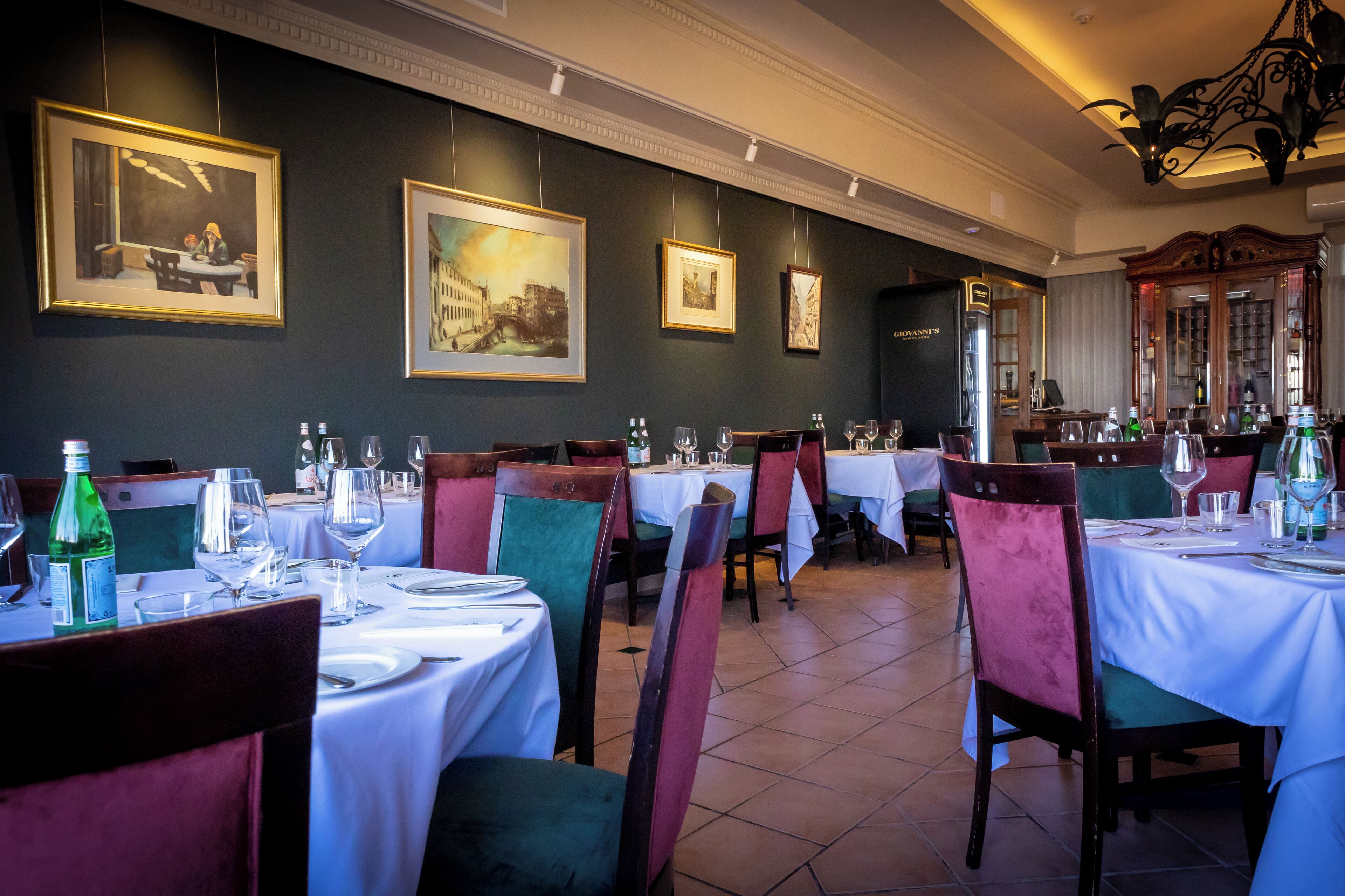 A restaurant with multiple tables set for dining, framed artwork on the walls, and a chandelier.