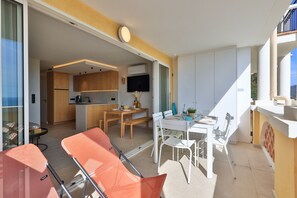 Una cocina moderna con armarios de madera, un comedor con mesa blanca y sillas naranjas, y un ventanal que proporciona luz natural.