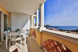 Un balcón con mesa y sillas, vista al mar y una montaña al fondo.