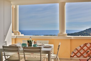 A dining area with a table set for two, overlooking a scenic view of the sea and a distant hill. - Appartement 3 Pièces vue sur mer (Saint-Raphaël)