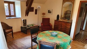 Un coin repas avec une table dressée pour deux personnes, un fauteuil rouge, un meuble en bois et un grand miroir.