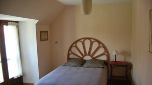 Une chambre à coucher avec un lit, une table de chevet avec une lampe, une fenêtre avec des rideaux et un tableau accroché au mur.